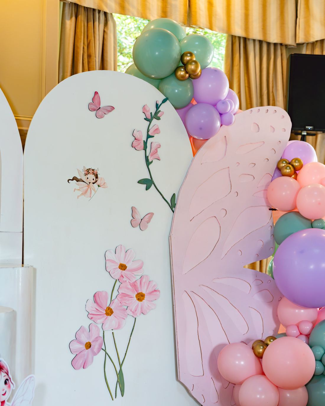 Hand-painted arch backdrop with butterfly wings and a pastel balloon garland