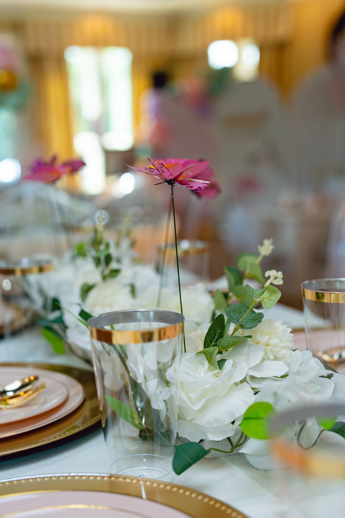 Table centrepiece of white florals, eucalyptus and a pink butterfly pick